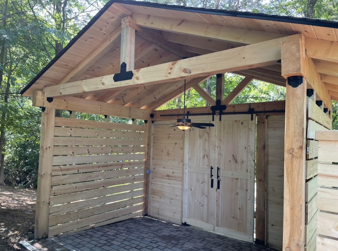 Wooden shed with double doors and covered porch in wooded backyard