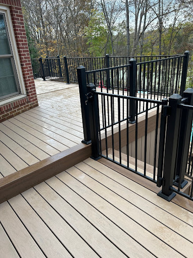 Wooden deck with black metal gate and railing, trees in background