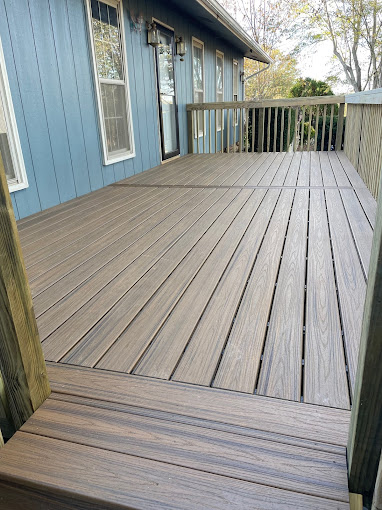 Wooden deck with gray boards attached to blue house with wooden railing