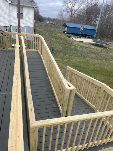 Wooden wheelchair ramp with gray decking leading to a white house