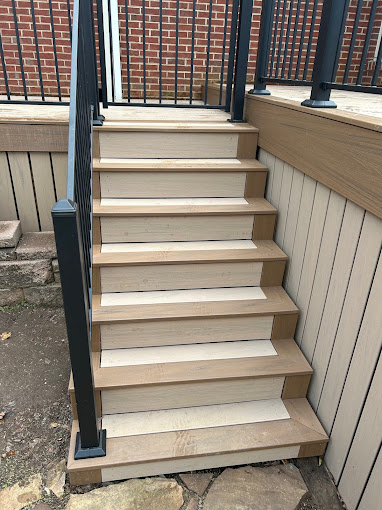 Wooden stairs with black metal railing leading up to a deck