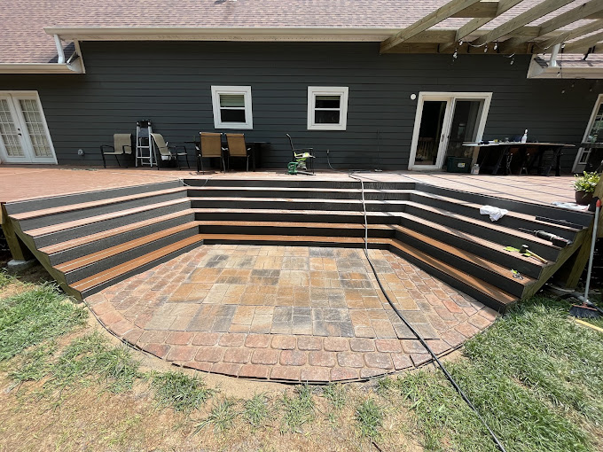 Multi-level wooden deck with stone patio and steps beside house