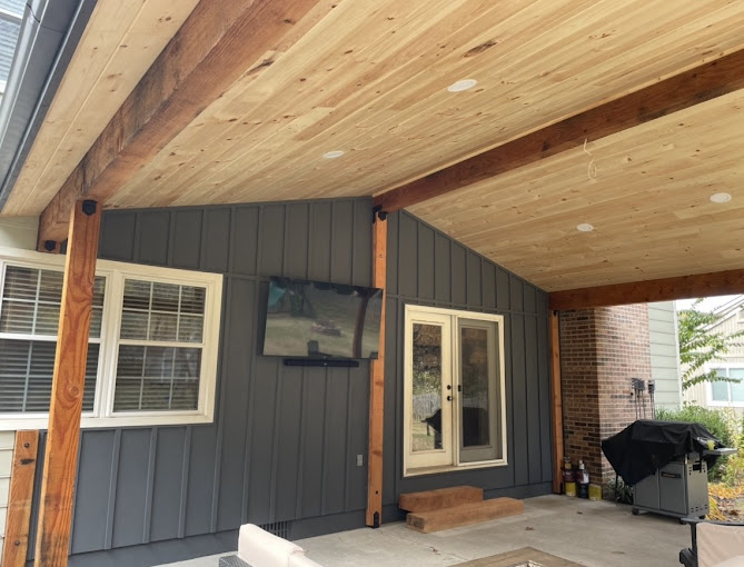 Modern patio with wooden ceiling, gray siding, and mounted TV near grill