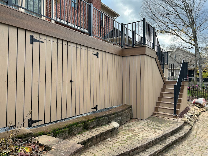 Wooden deck with metal stairs and railing, stone retaining wall and paver path