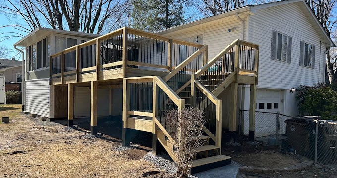 Wooden two-story deck attached to white suburban house with metal railings