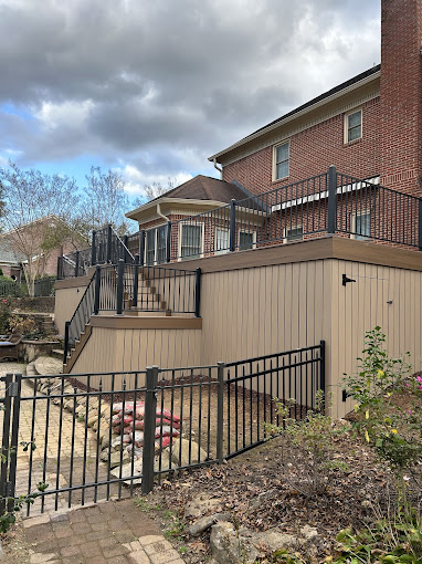 Multilevel wooden deck with black metal railings attached to brick house